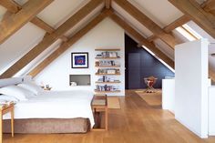 an attic bedroom with wood floors and white walls, along with wooden framed bookshelves