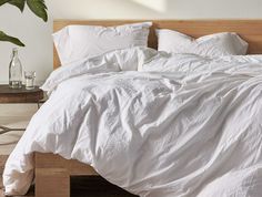 a bed with white linens and pillows in a minimalistic bedroom setting, along with a potted plant