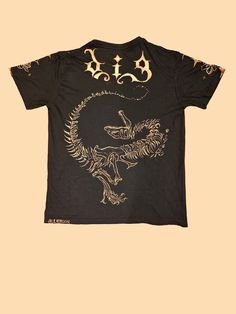 Get ready to stand out in style with this black tee featuring a striking dinosaur design! Hand-painted with bleach on soft cotton, it's a statement piece that's sure to turn heads. 🦖 The front depicts a dinosaur skull and a couple bone tails, while the back features a full skeleton with "DIG" in a gothic font. 🌟 Intricate flowers and stars adorn the sleeves, adding a touch of whimsy to this grunge-inspired shirt! 🌟 Men's U.S. Small 🌟 100% cotton 🌟 Relaxed fit Casual Acid Wash T-shirt With Skull Print, Black Dinosaur Print Short Sleeve T-shirt, Black Short Sleeve T-shirt With Dinosaur Print, Casual Dinosaur Print Tops For Streetwear, Black Dinosaur Print Crew Neck Top, Fitted Acid Wash T-shirt With Graphic Print, Cotton Dinosaur Print Tops For Streetwear, Acid Wash Skull Print Graphic Tee, Acid Wash Graphic Tee With Skull Print