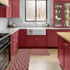 a kitchen with red cabinets and an oven in the center, along with a rug on the floor