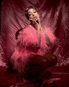 a woman sitting on the ground with her hands to her face and wearing pink feathers