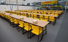 tables and chairs are lined up in a large room with yellow seats on the floor