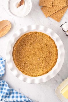 a pie crust in a white pie plate on a marble table with crackers and cheese