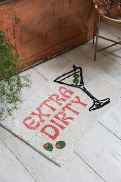 a white door mat with the words happy christmas and a wine glass on it next to a potted plant