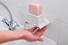 a person holding a soap dispenser in their hand over a sink faucet