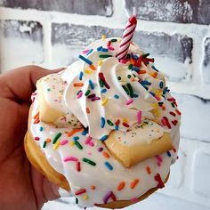 a hand holding up a frosted donut with sprinkles and a candle