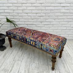 a bench sitting on top of a wooden floor next to a potted plant in front of a white brick wall