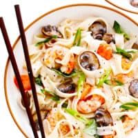 two plates filled with pasta and shrimp next to chopsticks on a white surface