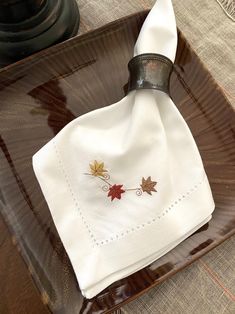 a white napkin on top of a wooden tray with an autumn leaf embroidered on it