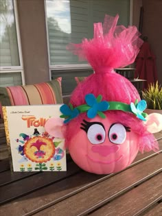 a pink troll pumpkin sitting on top of a wooden table next to a book and plant