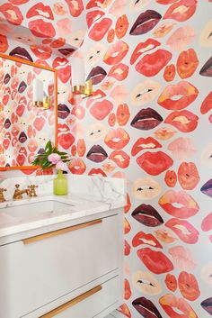 a bathroom with pink and orange lips on the wall, gold faucet, marble counter top