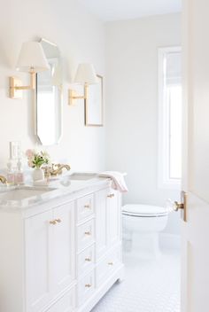 a white bathroom with gold accents and marble counter tops, along with a toilet in the background