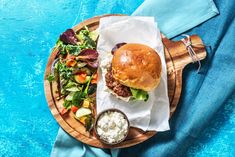 a burger and salad on a wooden platter