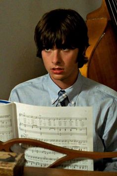 a young man sitting in front of an open book with sheet music on it and looking at the camera