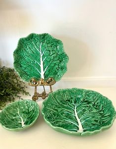 three green leaf shaped dishes sitting on top of a white table next to a potted plant