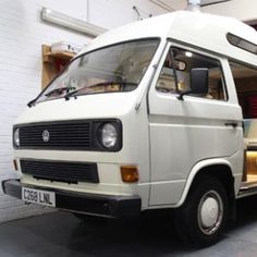 an old white van parked in front of a building with its doors open and people inside