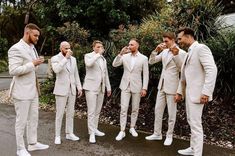 a group of men in white suits standing next to each other and taking pictures with their cell phones