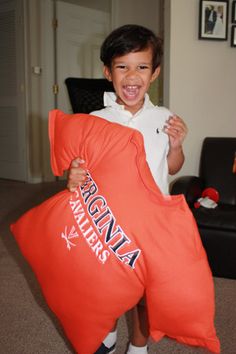 a young boy is holding an orange pillow