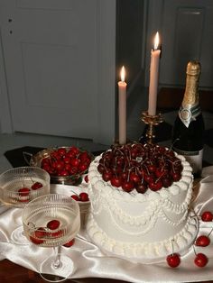 a white cake with cherries on it and two wine glasses sitting next to it