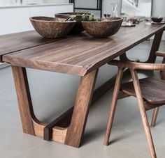 a wooden table with bowls on it and two chairs at the end, in front of a mirror