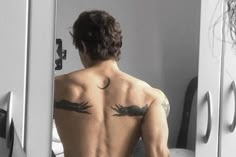 a man with tattoos on his back standing in front of a mirror