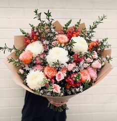 a person holding a bouquet of flowers in front of a brick wall