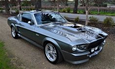 an old mustang muscle car parked on the side of a road in front of some trees