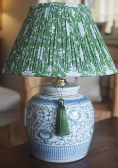 a blue and white vase with a green lamp shade on it's side, sitting on a table