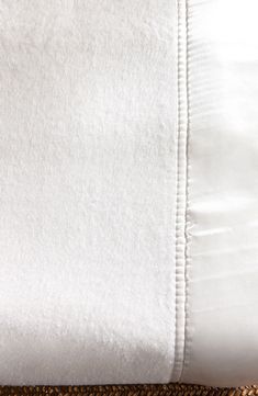 a close up of a white bed sheet and pillow on a brown mat with an orange flower