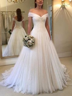 a woman standing in front of a mirror wearing a wedding dress with off the shoulder sleeves