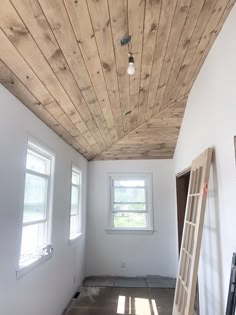 an empty room with wooden ceiling and ladder in the foreground, light coming through window