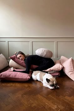 a woman is laying on the floor with pillows and a dog sleeping next to her