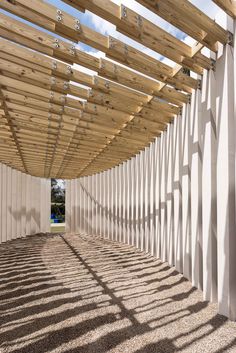 an empty walkway lined with white walls and wooden slatted roofing on the side of a building