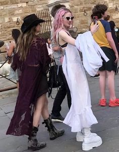 a woman with pink hair and white dress walking down the street in front of other people