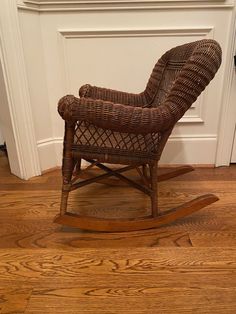 a wicker rocking chair sitting in front of a white wall and wood flooring