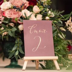 an easel with a sign on it and flowers in the background