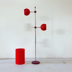 two red lamps are standing next to each other on the floor in front of a white wall