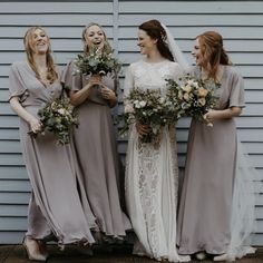 three bridesmaids are laughing together in front of a gray wall and holding bouquets