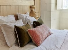 a bed topped with lots of pillows next to a wooden headboard in a bedroom