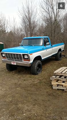 a blue and white truck parked on top of a dirt field next to wooden pallets