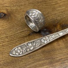 two silver spoons sitting on top of a wooden table next to a piece of wood