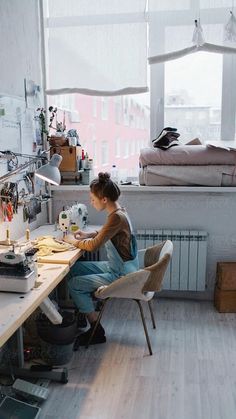 a woman sitting at a desk in front of a window working on a sewing machine