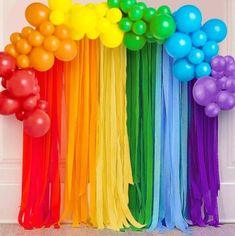 there are many balloons and streamers in front of the rainbow colored wall that is decorated with ribbons