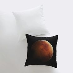 a black pillow with a red planet on it and two white pillows in front of it