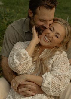 a man and woman cuddle together in the grass while they smile at each other