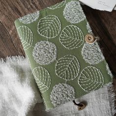 a green and white book with buttons on it sitting on a wooden table next to some fabric