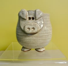 a ceramic piggy bank sitting on top of a clear plastic shelf against a yellow wall