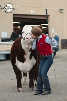 a woman is standing next to a brown and white cow with a stick in its mouth