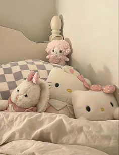 several stuffed animals are on the bed with white sheets and checkerboard wall behind them