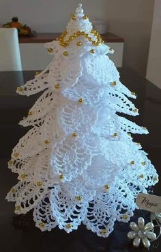 a white crocheted christmas tree sitting on top of a black table next to a flower